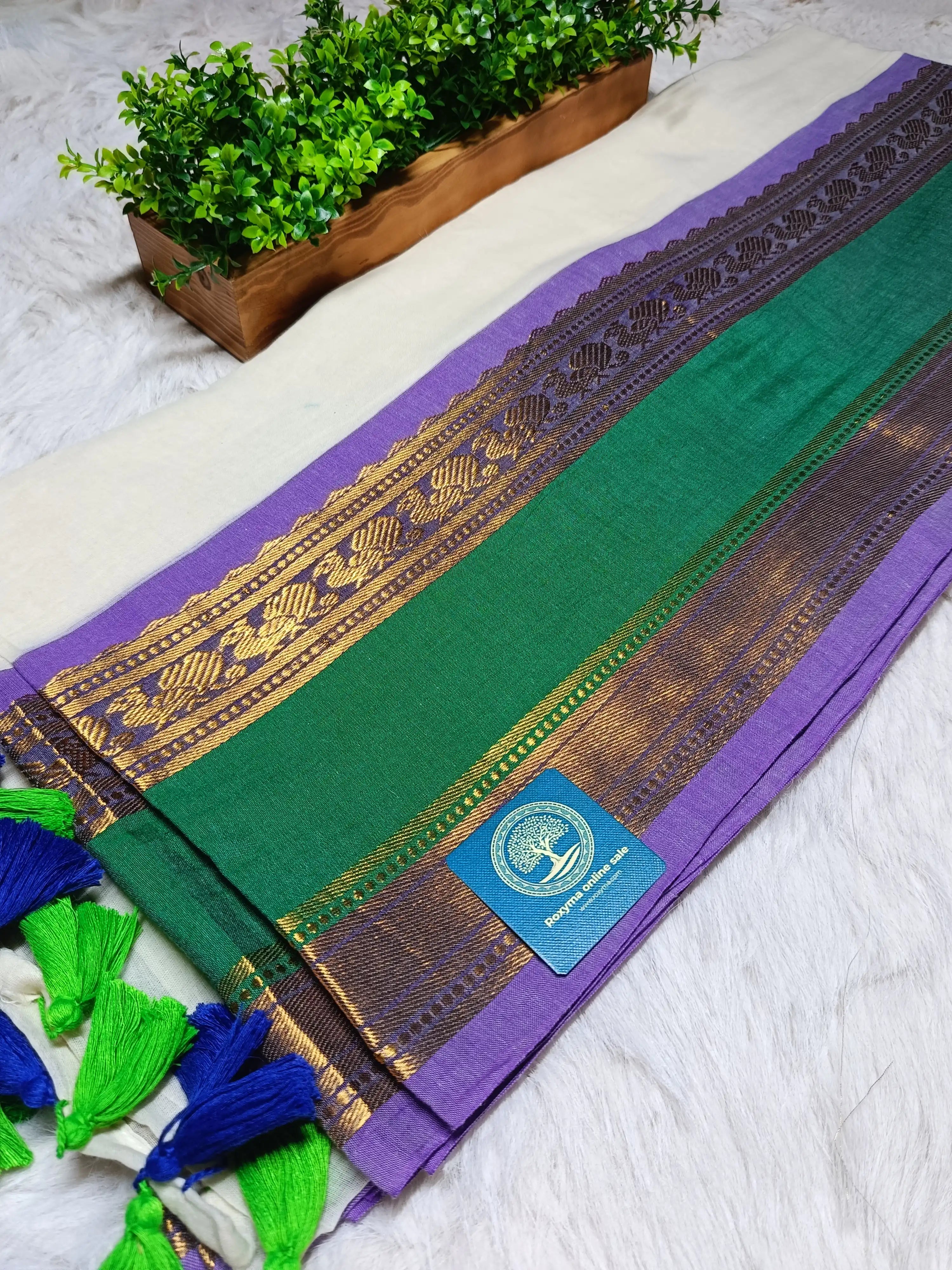 Green and purple traditional fabric with gold border and tassels on a white surface.