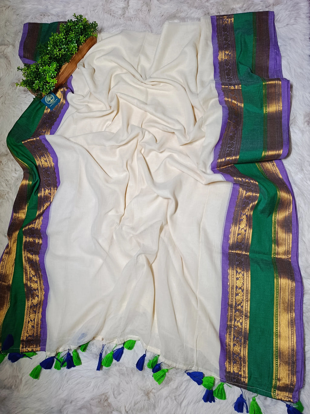 White saree with green and purple border on a textured surface