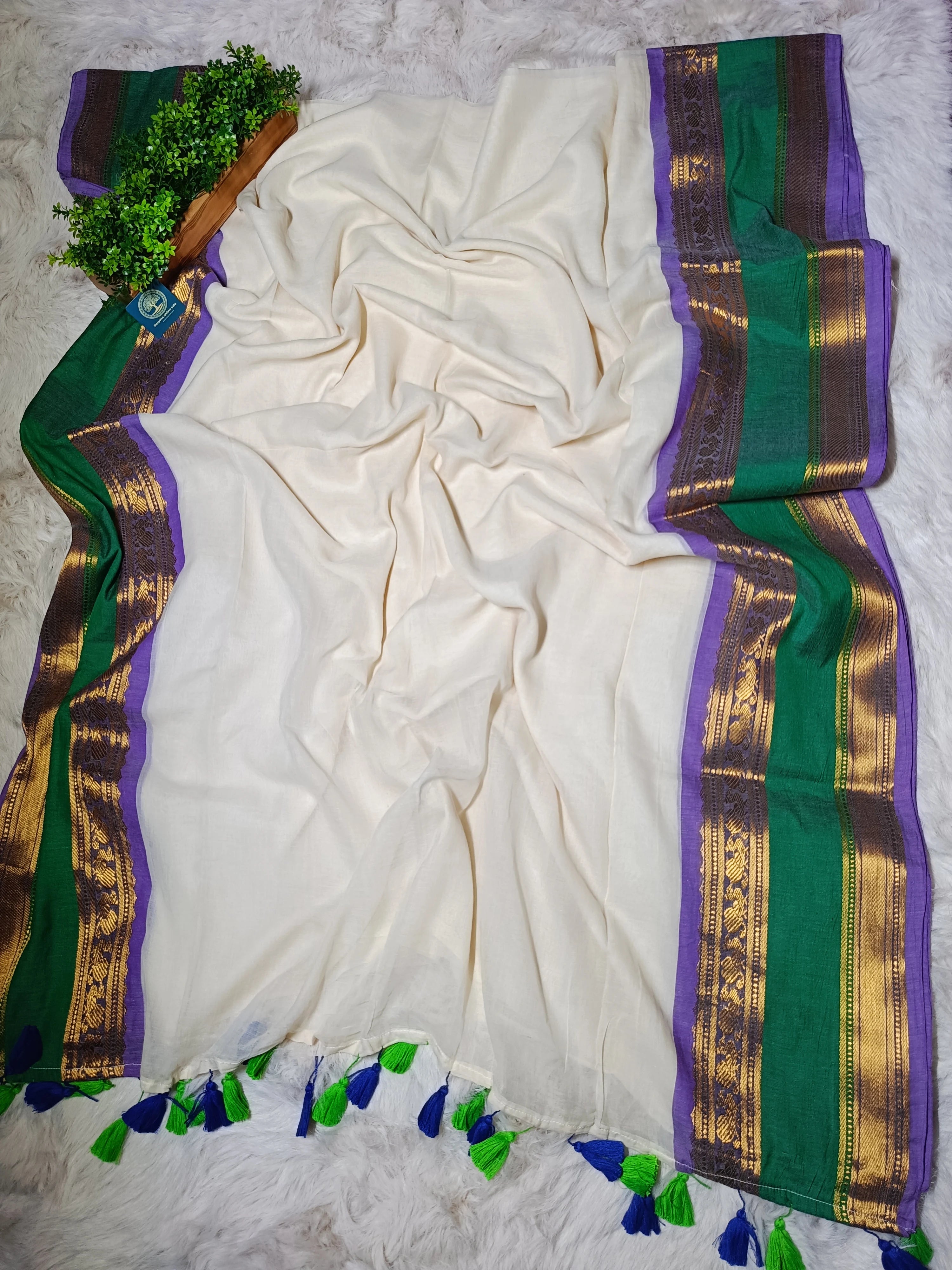 White saree with green and purple border on a textured surface